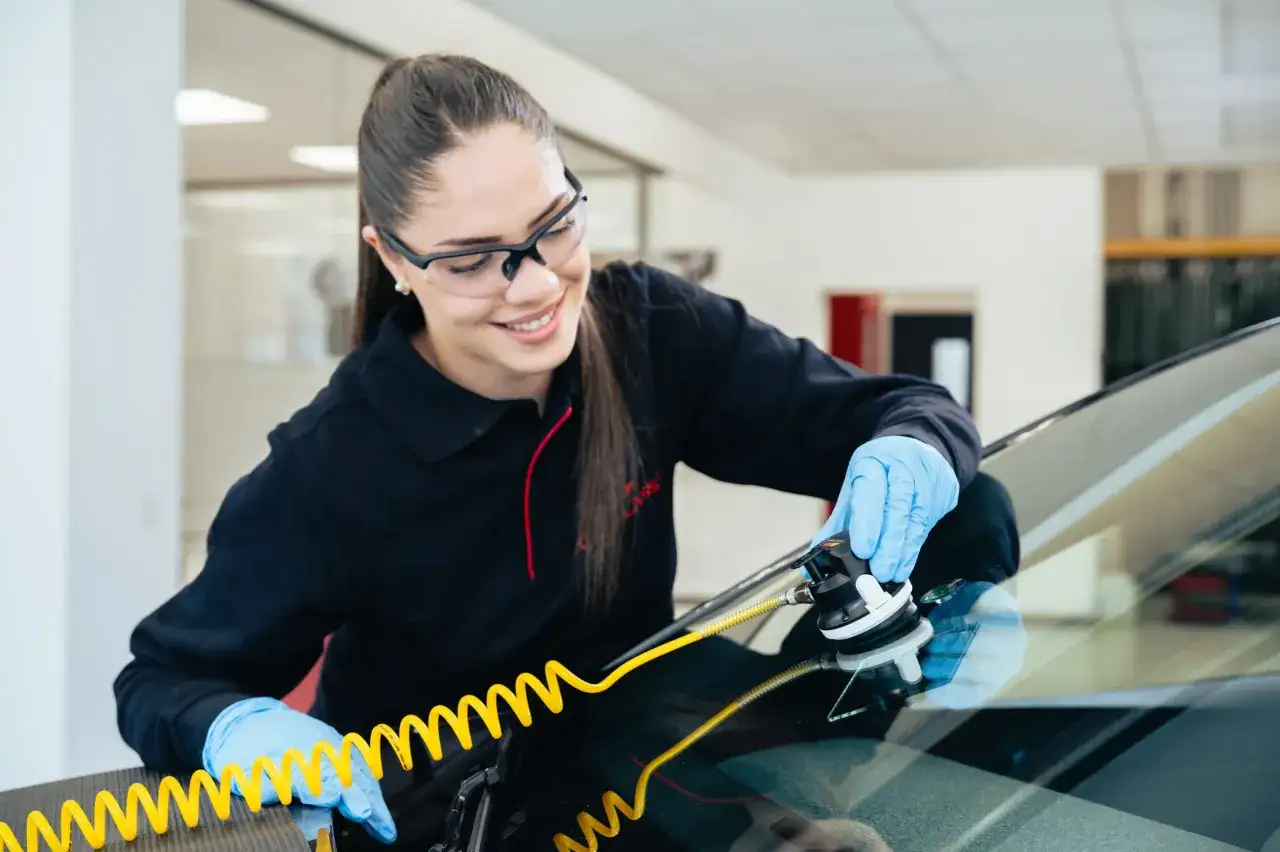 Technicienne souriante réparant un impact pare brise avec un kit spécialisé.