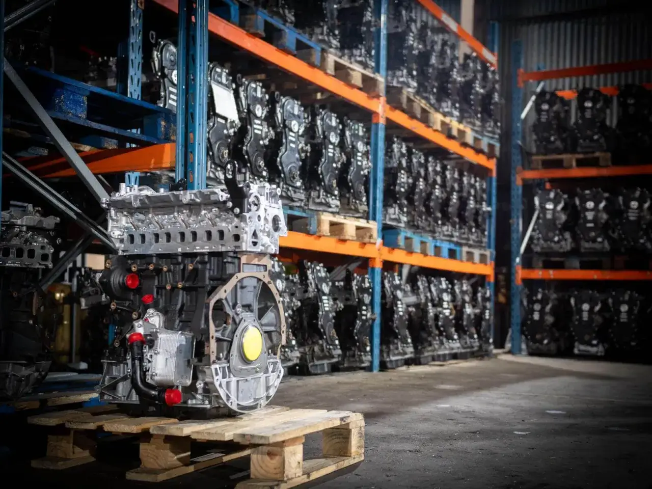 Un moteur automobile prêt pour un échange standard, aligné avec d'autres moteurs sur des étagères dans un entrepôt.