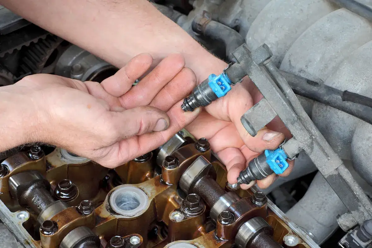 Mains d'un mécanicien manipulant des injecteurs de carburant pour un décalaminage moteur essence avis.