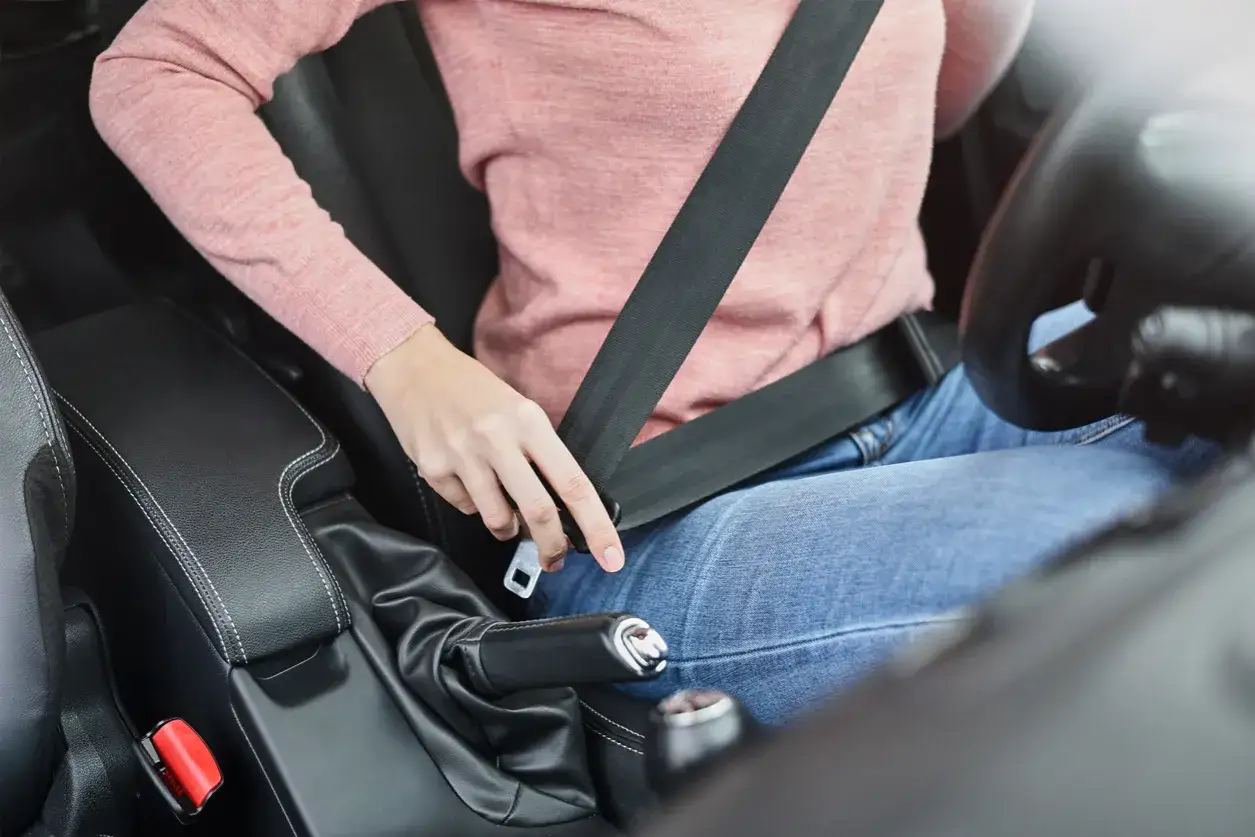 Une personne en jean et pull rose est sur le si&egrave;ge conducteur, pr&ecirc;te &agrave; changer ceinture de s&eacute;curit&eacute;.