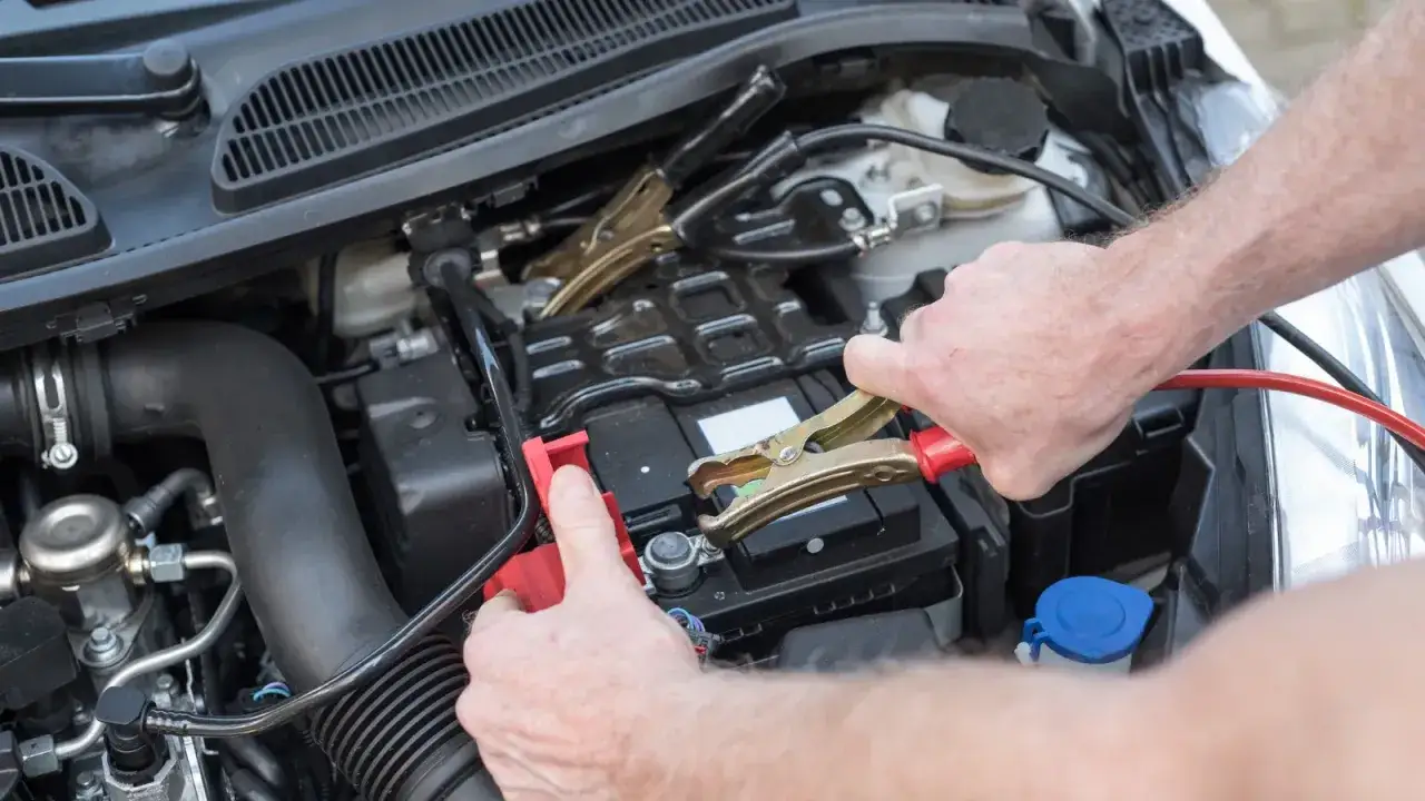 Mains de personne connectant des câbles de démarrage à une batterie de voiture pour la démarrer sans démarreur.