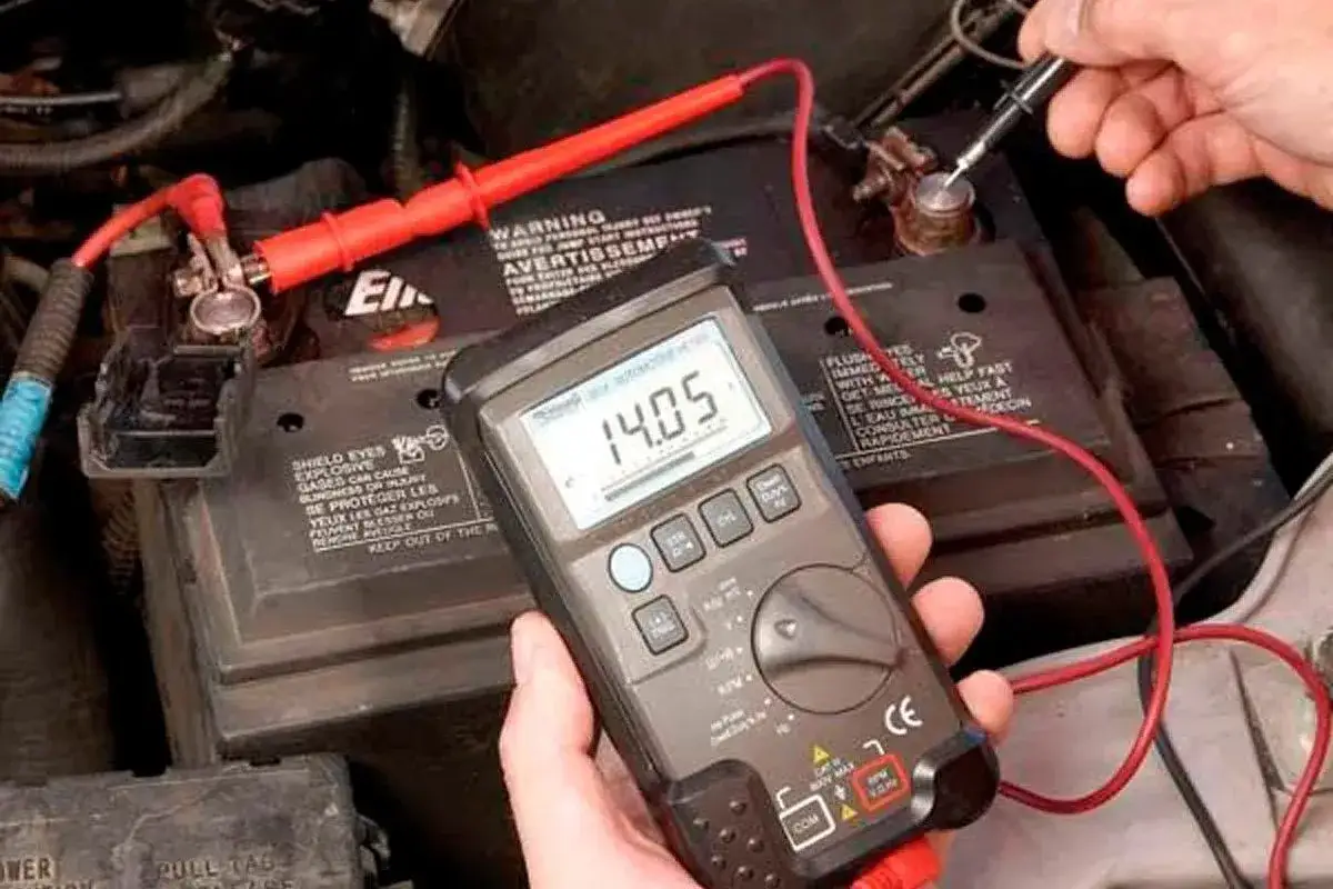 Comment tester un alternateur : un multimètre affiche 14.05V, connecté à une batterie de voiture avec des pinces rouges.