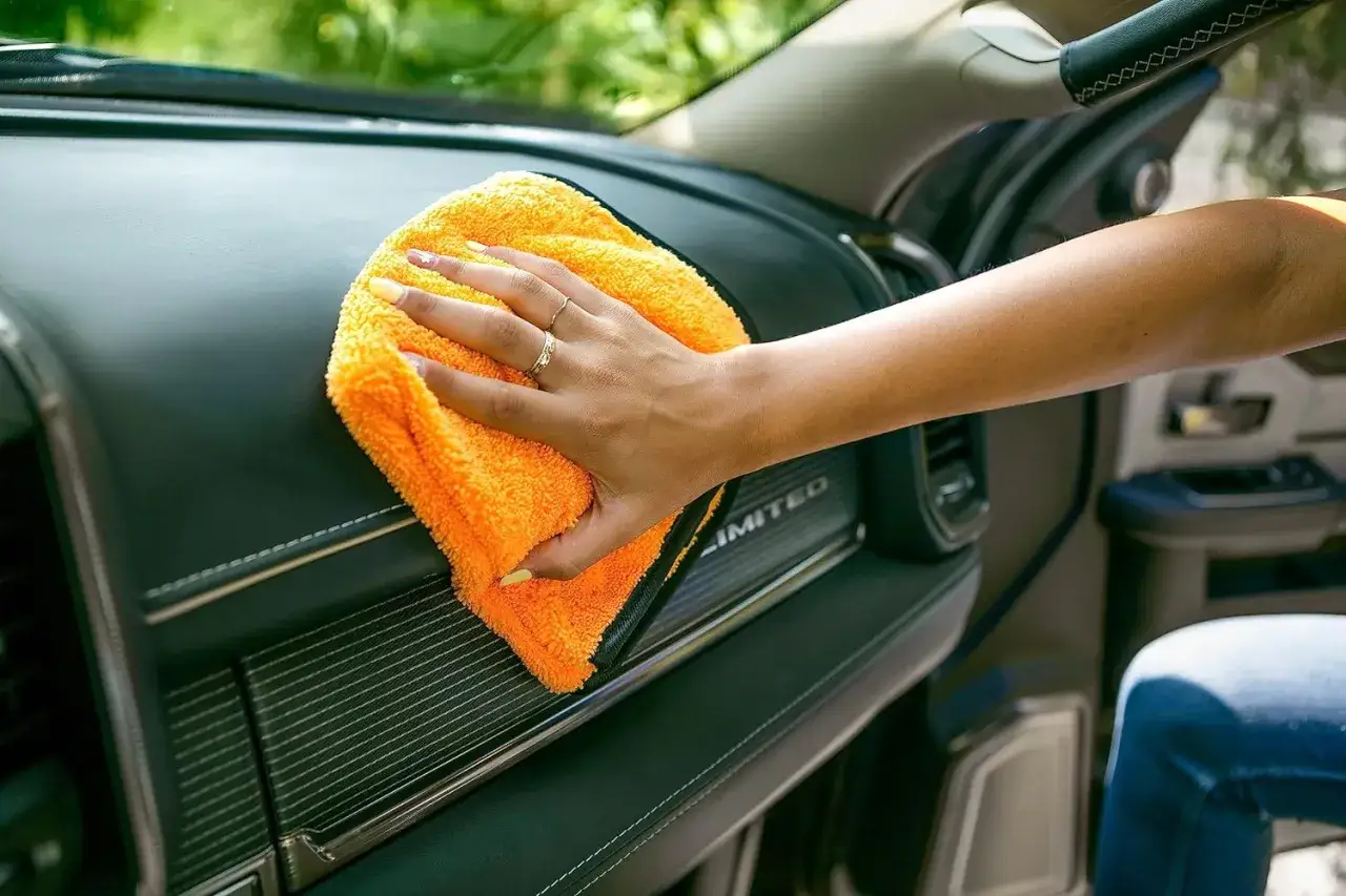 Main d'une personne nettoyant le tableau de bord d'une voiture avec un chiffon orange.