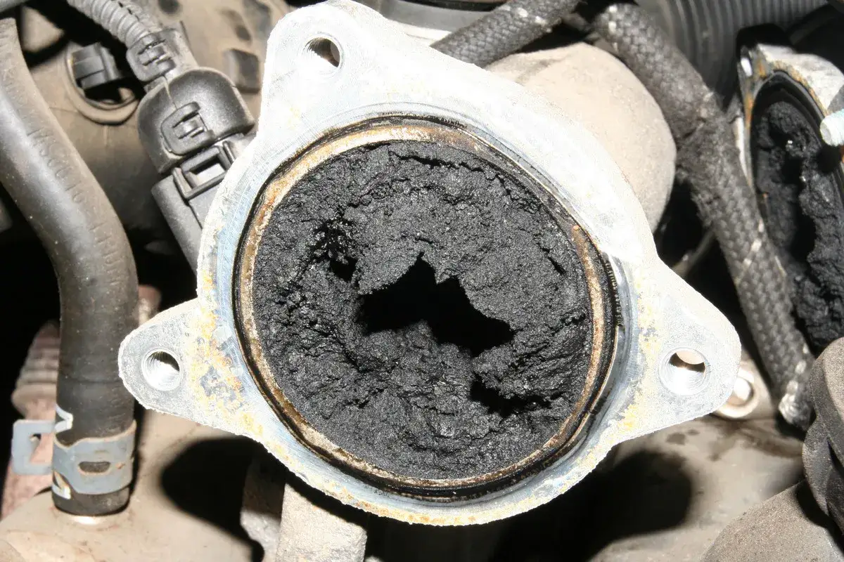 Gros amas de suie noire obstruant une pièce mécanique, signe d'un décalaminage moteur diesel nécessaire pour restaurer le flux.