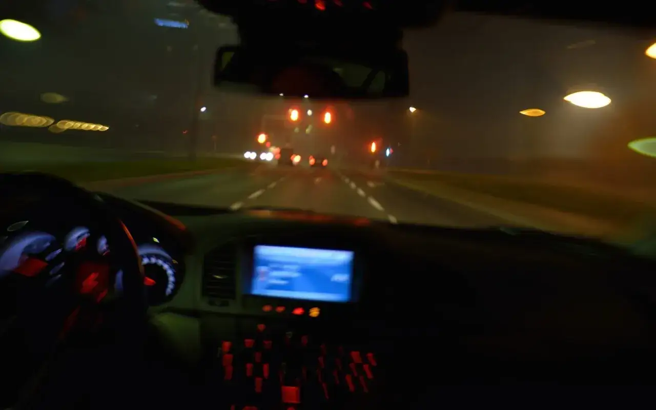 Vue depuis l'intérieur d'une voiture, la nuit. Les feux de route éclairent la chaussée mouillée, créant des traînées lumineuses.