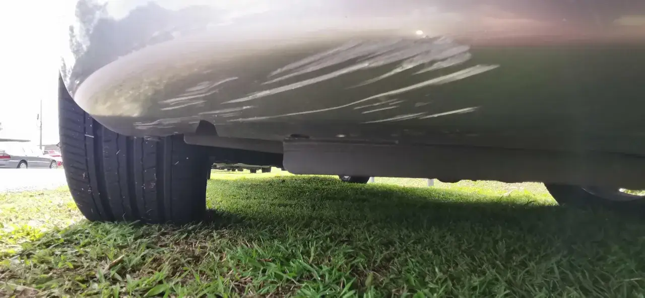 Vue basse du bas d'une voiture, montrant des éraflures sur le pare-chocs, probablement dues à un frottement voiture parking.