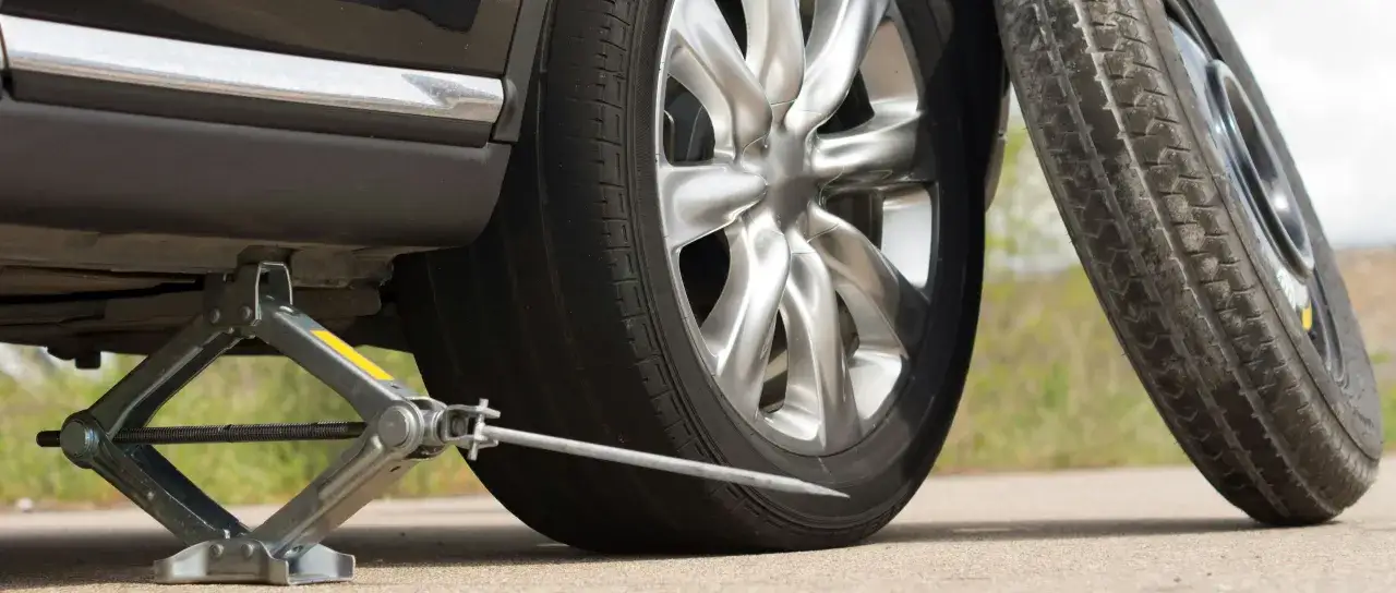 Un cric soulève une voiture pour changer un pneu crevé. La roue de secours est prête.