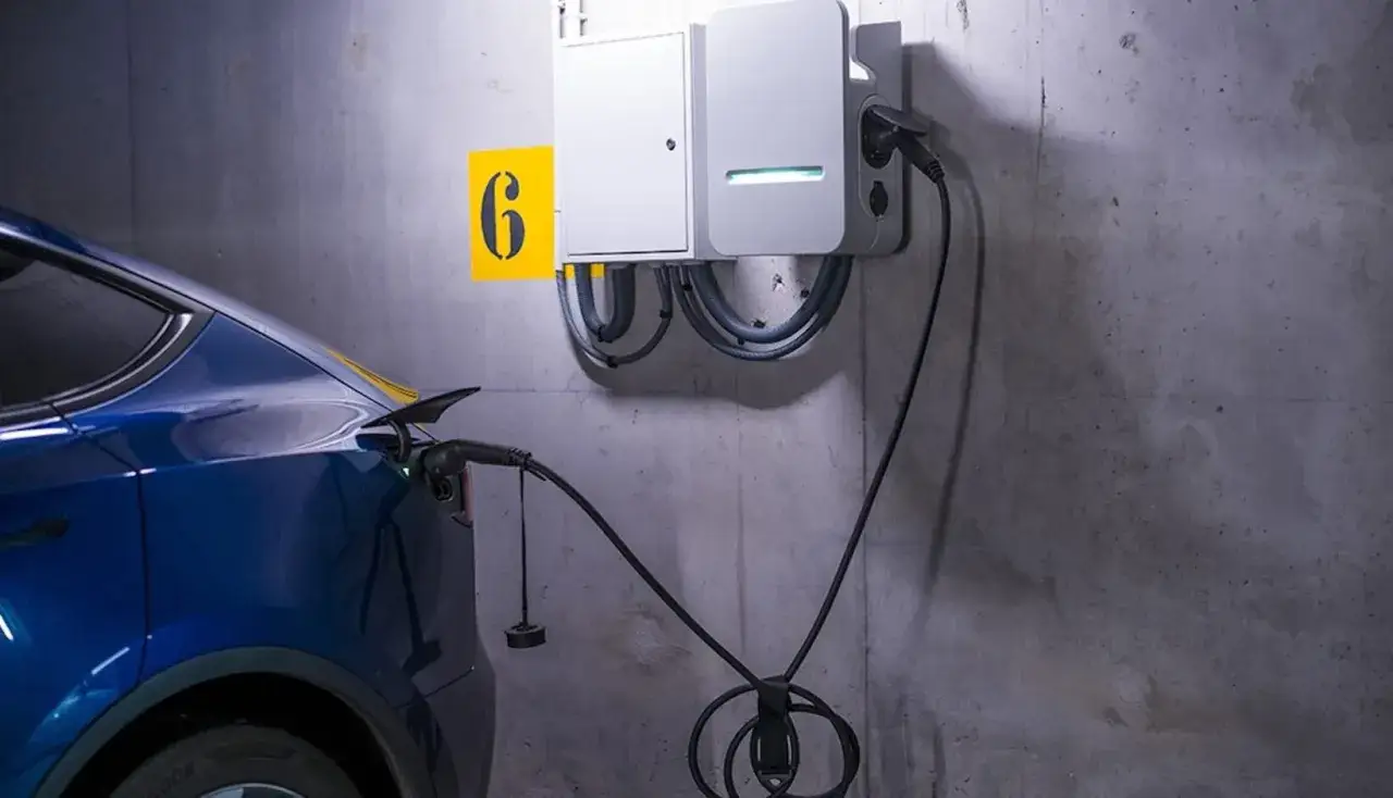 Une voiture électrique bleue est branchée à une borne de recharge murale. Le numéro 6 est affiché sur un panneau jaune.
