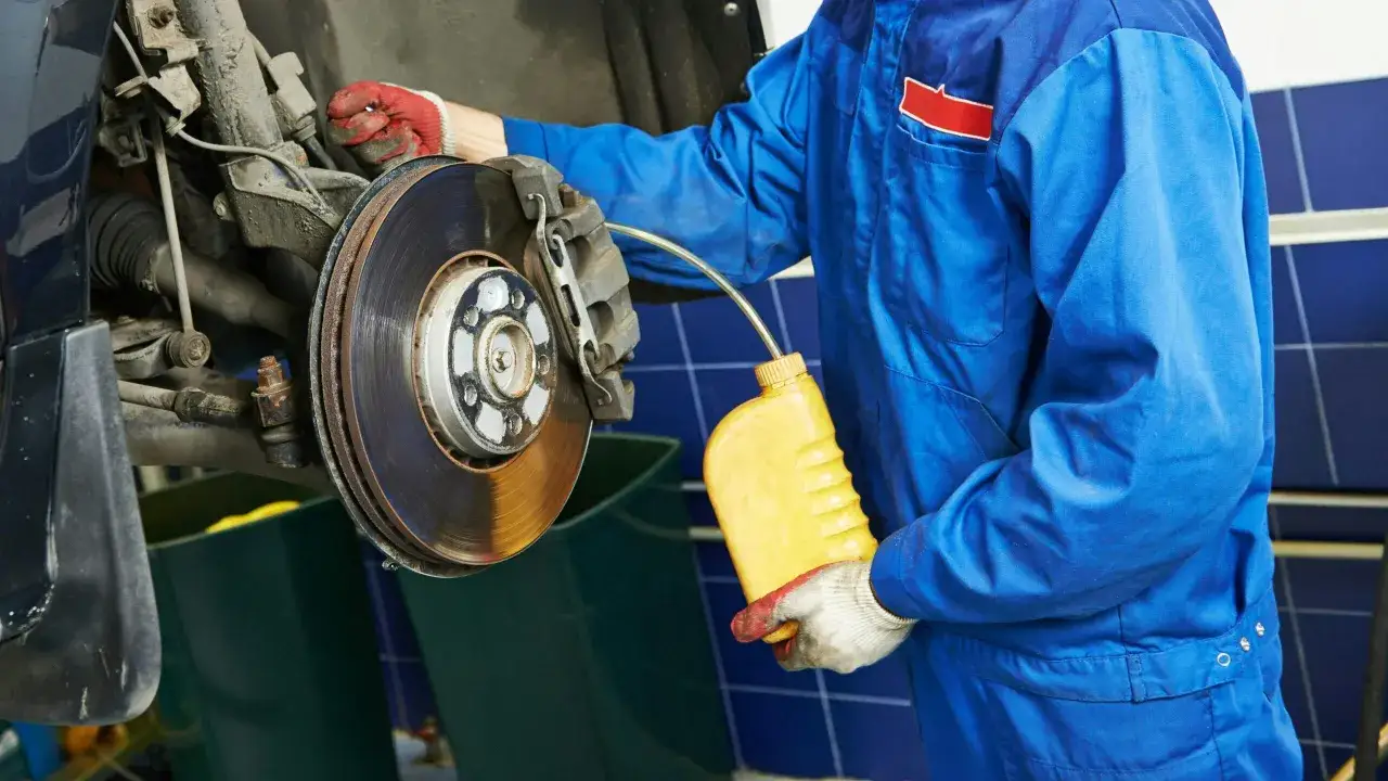 M&eacute;canicien en bleu, gants rouges, remplissant le liquide de frein. Le prix du changement de liquide de frein est une op&eacute;ration d'entretien essentielle.