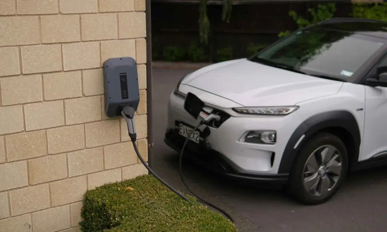 Borne de recharge murale connectée à une voiture électrique blanche. La question est : combien de kWh pour recharger une voiture électrique ?